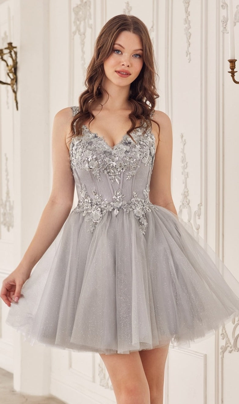 A woman in the Sequin-Corset Short A-Line Homecoming Dress CY019, a sleeveless gray tulle dress with floral embellishments, stands indoors against an ornate white wall.